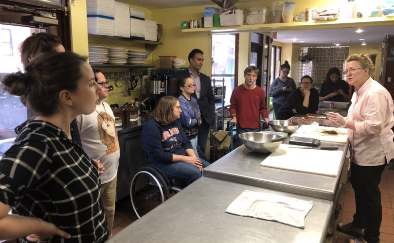 Mentors and mentees listening to Chef Napoli in a kitchen at the start of workshop.