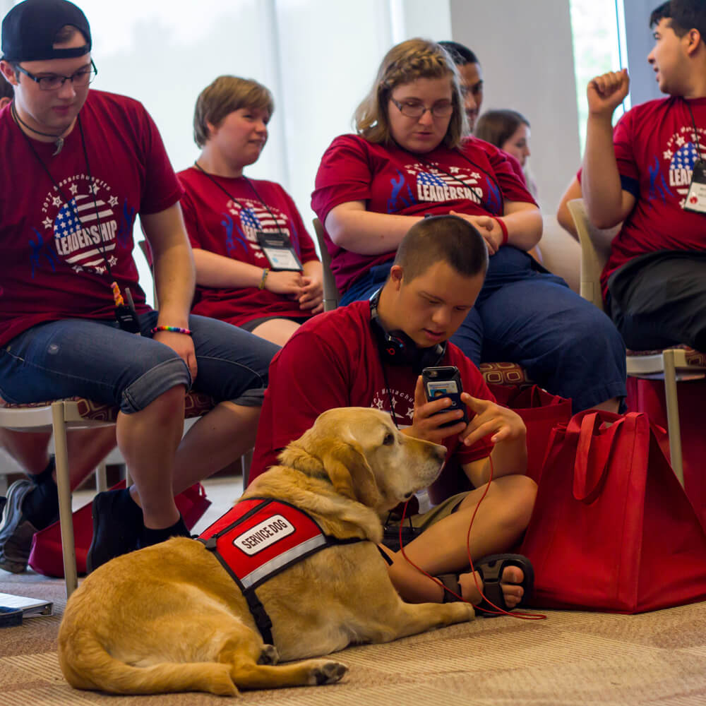A group of student and a service dog meeting at a leadership conference