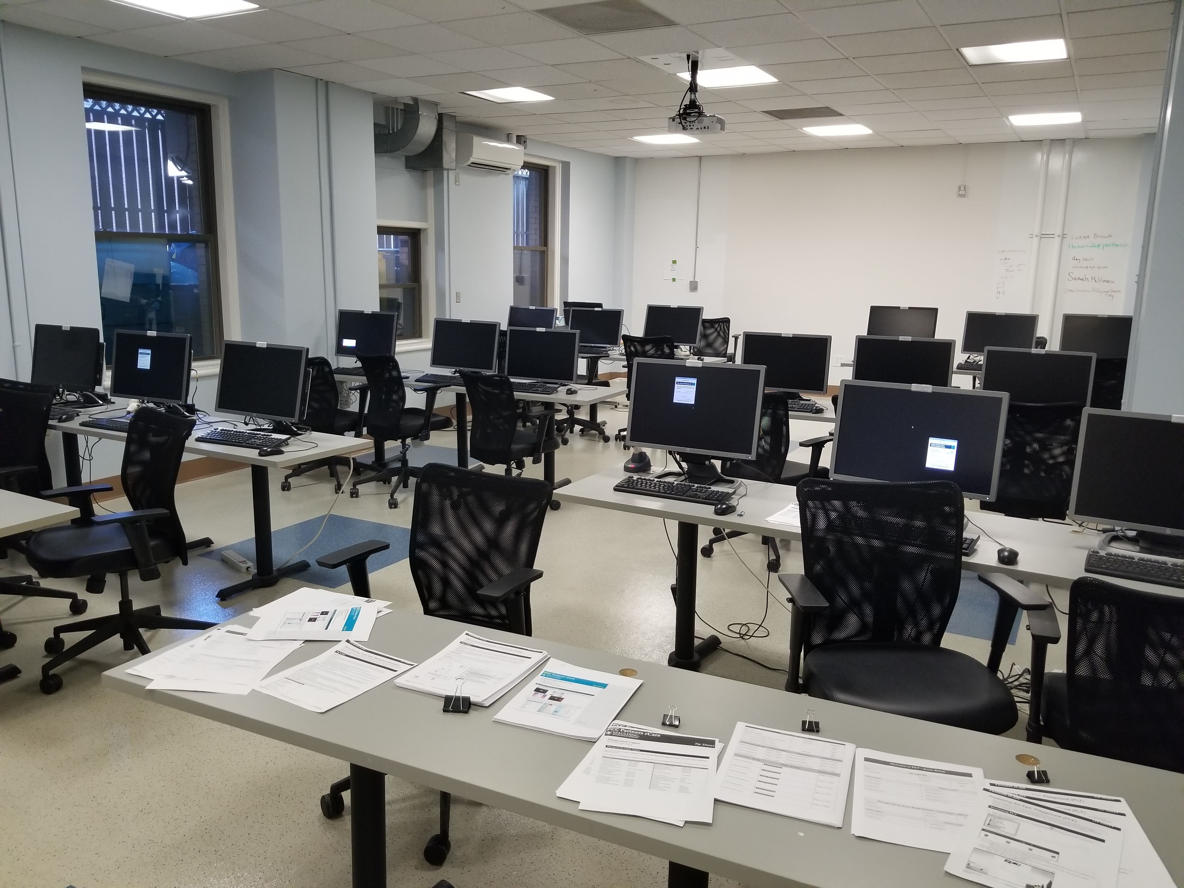 A classroom-style room with rows of tables and chairs, with computers at more desk spots.
