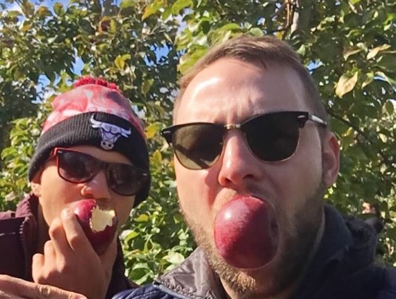 Matt and his mentee take a selfie while apple picking, both with apples in their mouths.