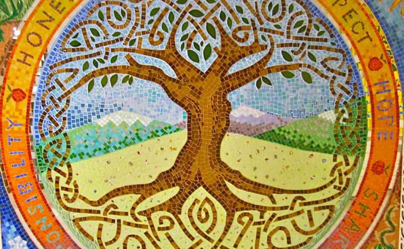 A colorful mosaic of a tree with long, intertwining roots and branches. In the background of the mosaic there is a mountain range.